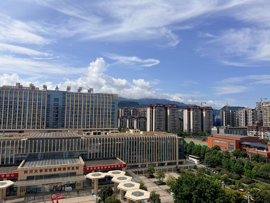 A panoramic view of a contemporary hospital and urban buildings in Sichuan under a bright blue sky.